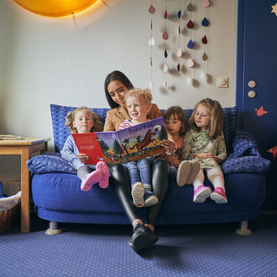Erziehern sitzt mit Kindern auf einem Sofa und zeigt ein Bilderbuch